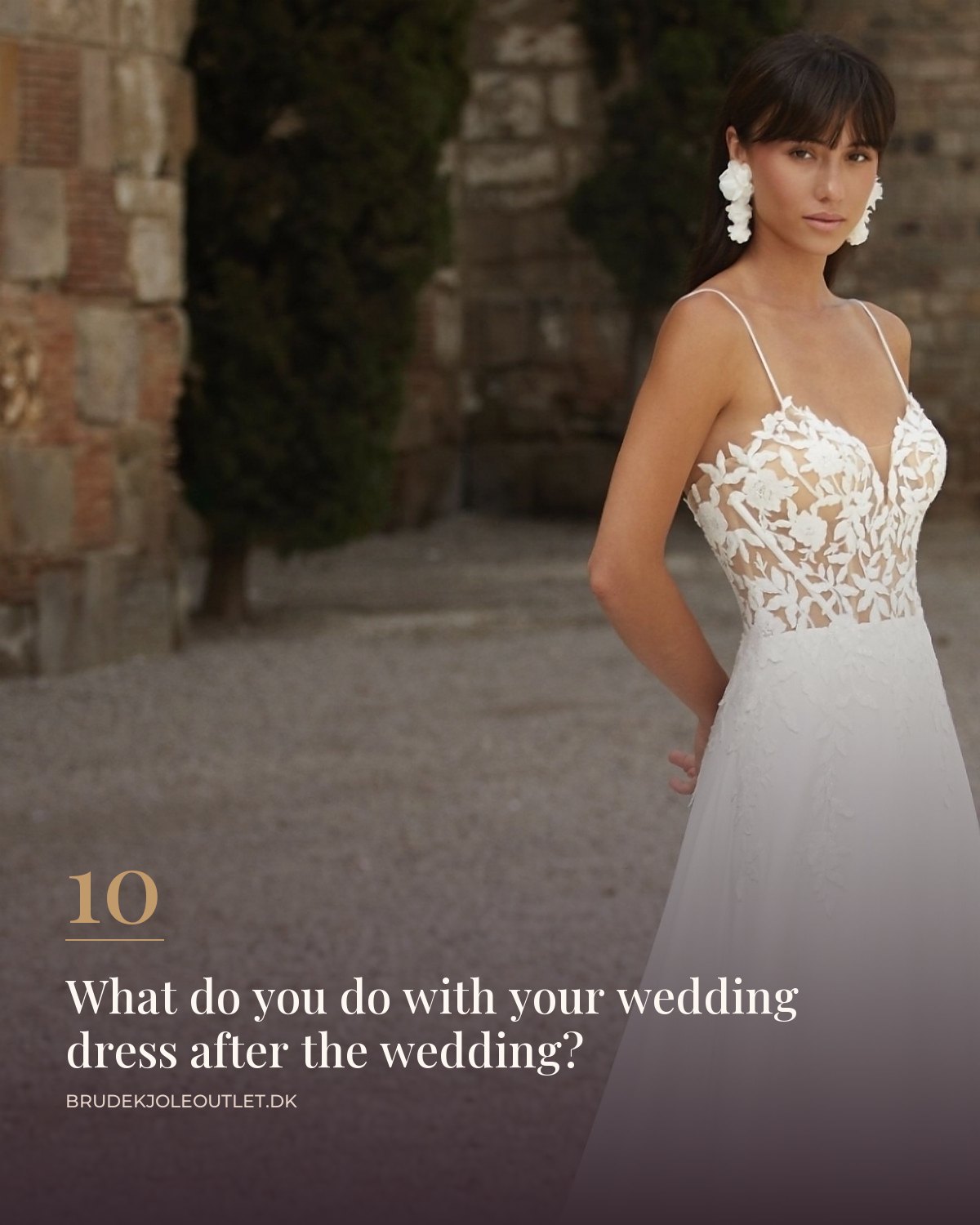 Wedding dress with thin straps, lace bodice and a long train outdoors by an old wall